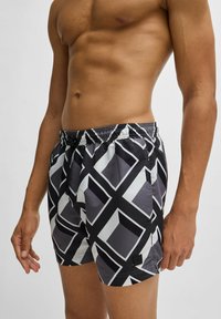 Shorts de bain à motif noir et blanc avec un design géométrique, taille élastique et cordon de serrage. Texture lisse et détail du logo à l'ourlet.