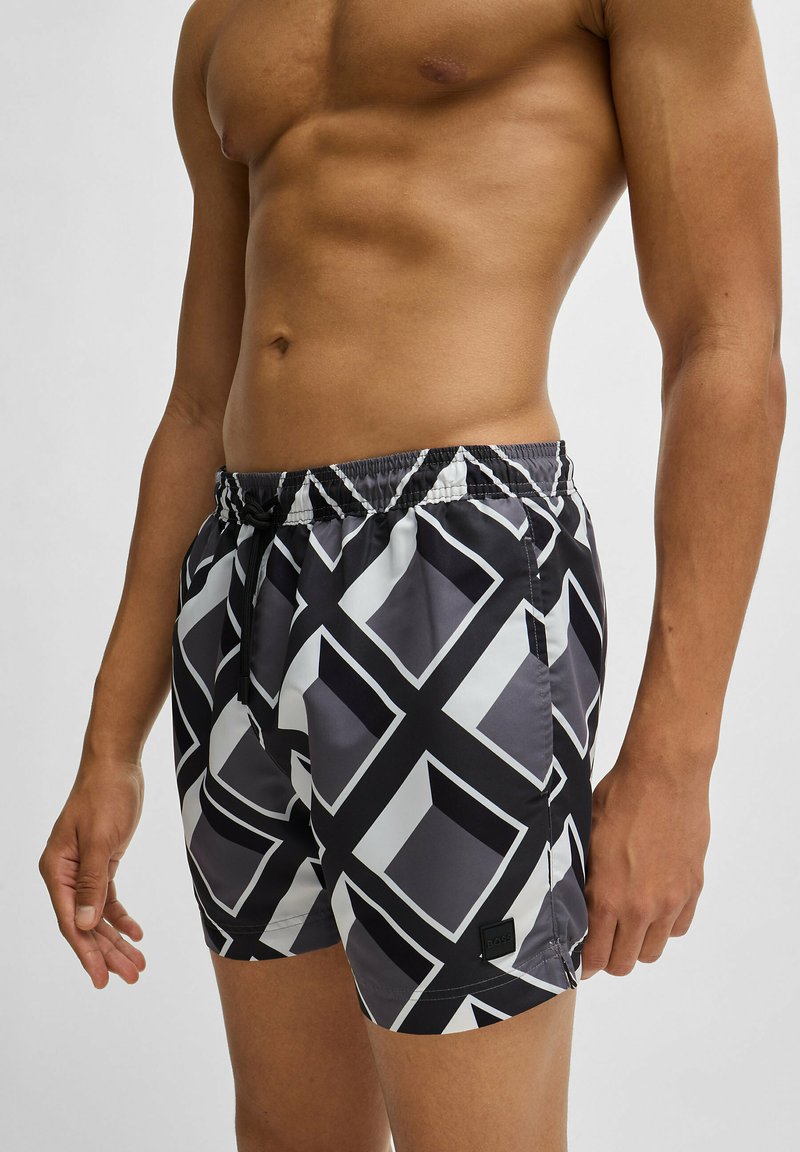 Shorts de bain à motif noir et blanc avec un design géométrique, taille élastique et cordon de serrage. Texture lisse et détail du logo à l'ourlet.