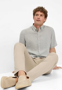 Kurzärmliges, hellgraues Hemd mit Knopfverschluss und kariertem Muster, kombiniert mit beigen Slim-Fit-Hosen und hellbraunen Slippern.