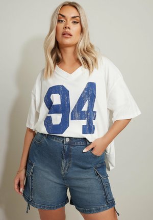 Weißes V-Ausschnitt-T-Shirt mit blauer, abgenutzter "94"-Druck, kombiniert mit blauen Jeans-Cargo-Shorts mit Seitentaschen und klassischer Passform.