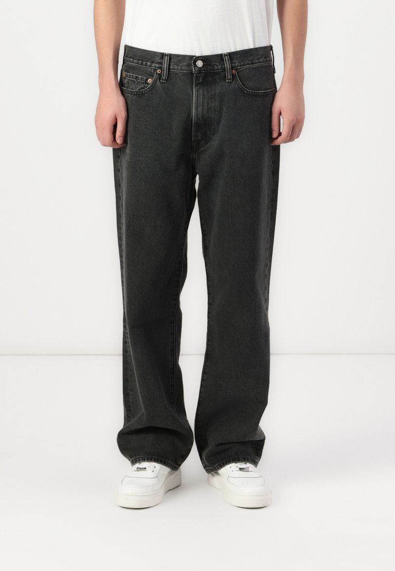 Mustmust värvi denim teksad lõdva istuvusega ja sirge säärega. Omab viit taskut, metallnuppu ja kontrastset õmblust. Kantud valgete tossudega.