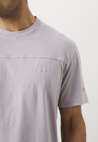 Lila Baumwoll-T-Shirt mit Rundhalsausschnitt, das ein erhabenes Logo auf der Brust und einen kleinen Logo-Akzent am Ärmel aufweist. Legerer Schnitt.