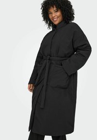 Melnā pufu jaka ar sašaurinātu jostas vietu, augstu apkakli un divām priekšējām kabatām; izceļas ar vienkāršu, funkcionālu dizainu un gludu tekstūru.