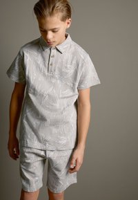 Graues Baumwoll-Polo mit kurzen Ärmeln, einem Blättermuster und einer geknöpften Kragenpartie, kombiniert mit passenden Shorts, die eine strukturierte Oberfläche aufweisen.