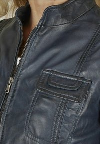 Tmavě modrá kožená bunda s přiléhavým límcem, zipovým zapínáním a dekorativní náprsní kapsou s vrstvenými šicími detaily.