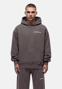Grijze hoodie met witte tekstlogo, buidelzak en geribbelde manchetten. Soepele stof, relaxed fit, gecombineerd met bijpassende broek.