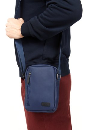 Borsa a tracolla blu navy con superficie testurizzata, forma rettangolare, chiusura con zip e tracolla regolabile, indossata di lato.