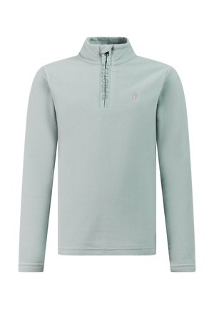 Jongen staat en draagt een lichtblauwe fleece met een kwart ritssluiting, zwarte broek en zwarte schoenen tegen een effen lichte achtergrond.