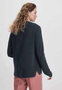 Tummansininen neulottu neulepaita, jossa on tekstuuripinta, pitkät hihat ja sivuhalkiot; yhdistetty vaaleanpunaisiin housuihin.