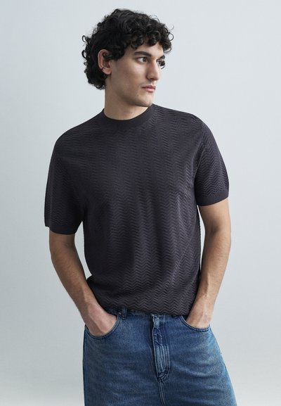 Short-sleeve, dark gray textured knit shirt with a round neckline, paired with blue denim jeans. The shirt features a subtle zigzag pattern.