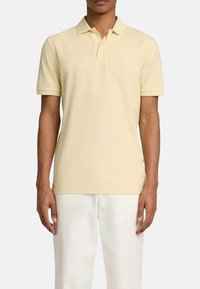 Polo en jaune pâle, manches courtes, col classique, fabriqué en tissu coton doux, avec un ourlet droit et un logo subtil sur l'ourlet.