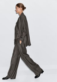 Gray pinstriped suit set featuring a double-breasted jacket and wide-leg trousers, paired with black shoes. Smooth fabric and relaxed fit.