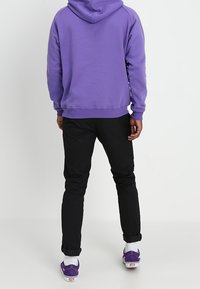 Fialová mikina s kapucí a žebrovanými cuffami, kombinovaná s černými slim-fit kalhotami a fialovými teniskami. Bavlněný materiál, ležérní design.