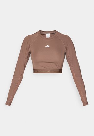 Haut court à manches longues marron en tissu lisse et extensible. Présente un col rond et un logo blanc contrastant sur la poitrine.