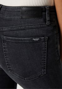 Tummat farkut, joissa on tiukka muotoilu. Vyötäröllä nahkaleima ja takataskussa pieni brändilogo.