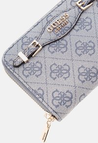 Helleblaue Geldbörse im Denim-Muster mit goldenen Beschlägen, ausgestattet mit einem Reißverschluss und detaillierten Akzenten, mit eingeprägtem Logo auf der Vorderseite.