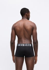 Boxer briefs neri con un logo bianco di Calvin Klein sulla vita, caratterizzati da una texture liscia e un design aderente. Modello girato di lato.
