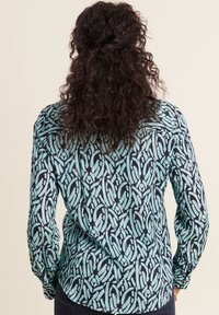 Langarmshirt met een geometrisch patroon in teal en marineblauw, gemaakt van lichtgewicht stof met een soepele textuur en met knoopmanchetten.