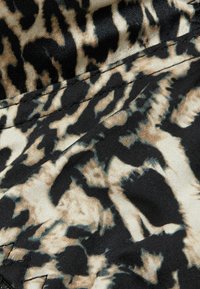 Tissu à motif léopard dans des tons noirs, beiges et bruns. Texture lisse avec des tourbillons de couleur. Détails de couture visibles le long des bords.