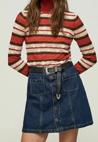 Röd och krämfärgad randig stickad tröja med hög hals, kombinerad med en mörk denim A-linjekjol med framknappar och ett svart bälte.