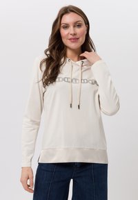 Lichtbeige hoodie met een trekkoord, met een zilveren kettingontwerp op de borst. Zacht stof en lange mouwen met een relaxte pasvorm.