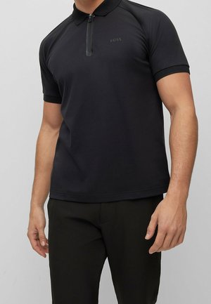 Schwarzes Poloshirt mit kurzen Ärmeln, Reißverschluss am Kragen und kontrastierenden Nähten, aus glattem Stoff. Logo-Detail auf der Brust eingearbeitet.