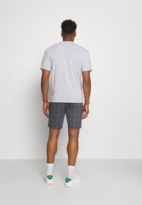 T-shirt grigia a maniche corte con scollatura rotonda, abbinata a pantaloni corti scuri a fantasia. Dettagli notevoli includono calze e scarpe da ginnastica bianche.