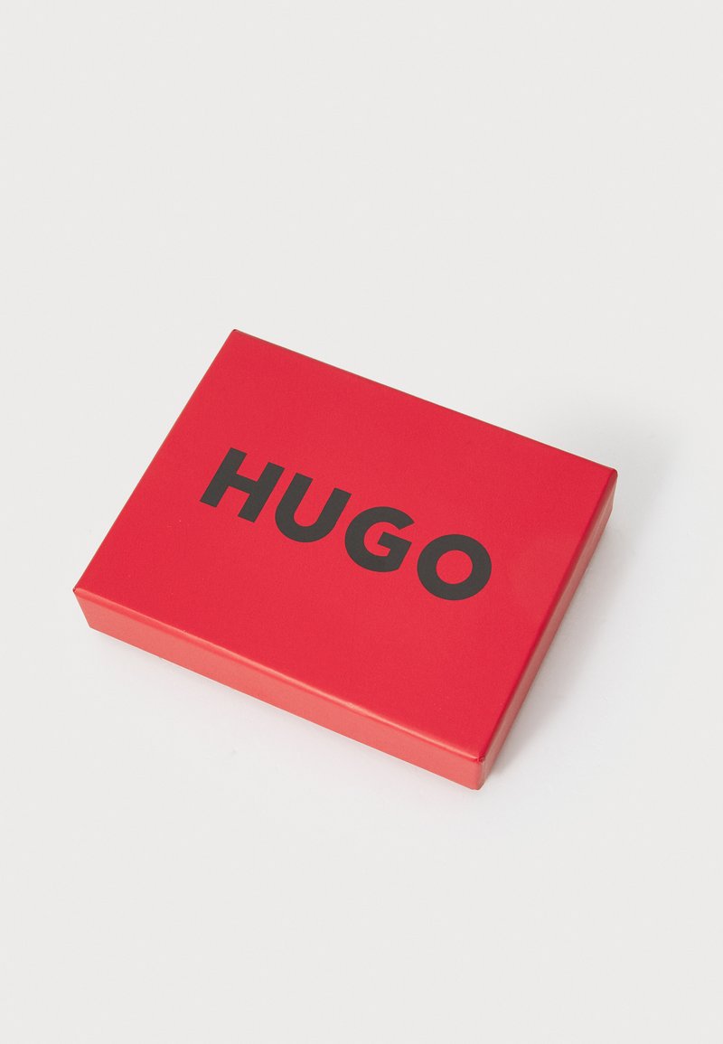 Rote Pappschachtel mit glänzender Oberfläche, auf der Oberseite in fetter schwarzer Schrift "HUGO" geschrieben. Schlichte rechteckige Form.