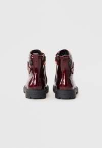 Bottes en cuir laqué bourgogne avec semelles en caoutchouc noires, dotées d'un détail de patch floral et de fermetures éclair sur le côté pour un enfilage facile. Texture lisse.