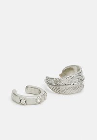 Anillos de plata con un diseño de hoja texturizada y una banda más pequeña con tres acentos de piedras transparentes. Acabado de metal suave, estilo de extremos abiertos.