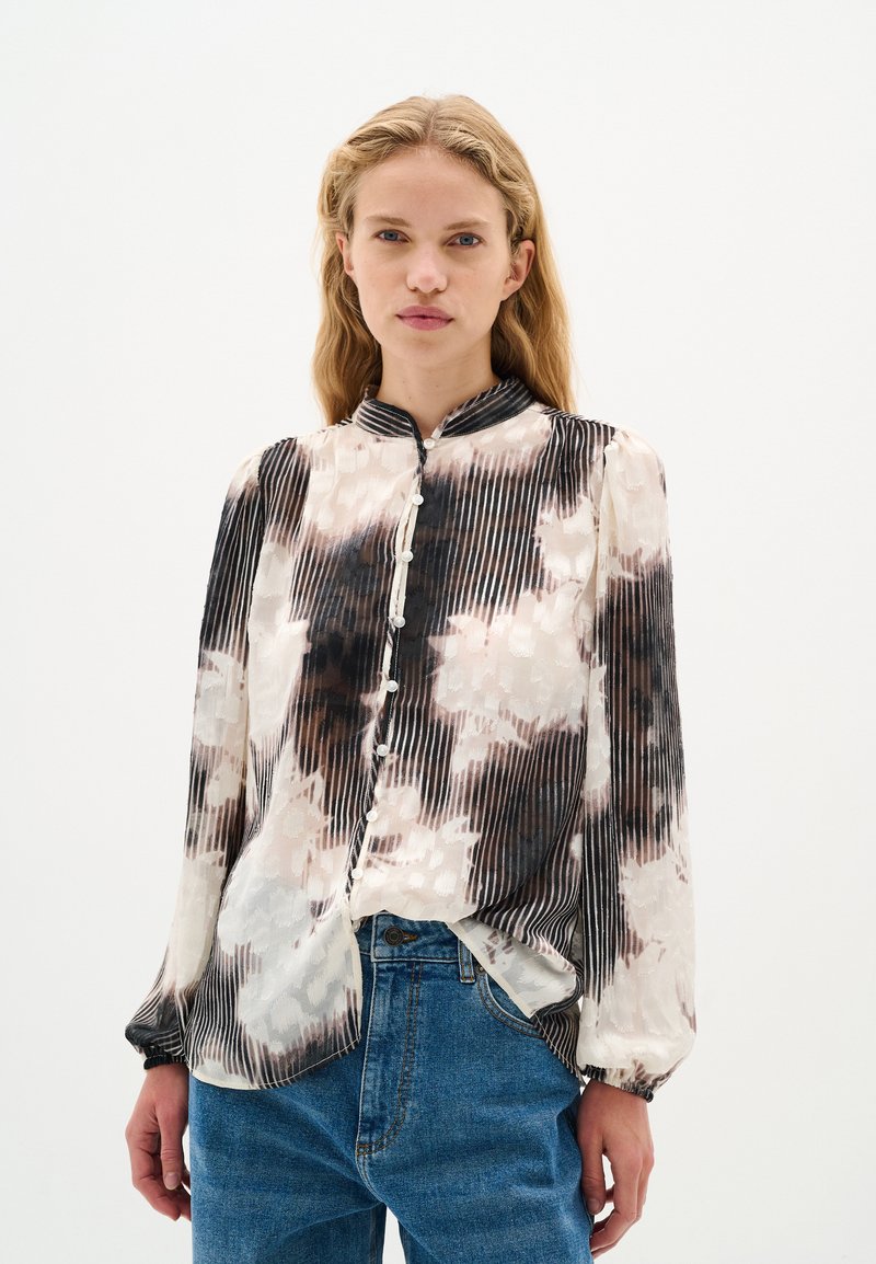 Bluza z dolgimi rokavi iz svile, ki ima črno-belo tie-dye vzorčenje z navpičnimi črtami, mandarin ovratnik in gumbasto zapiranje.