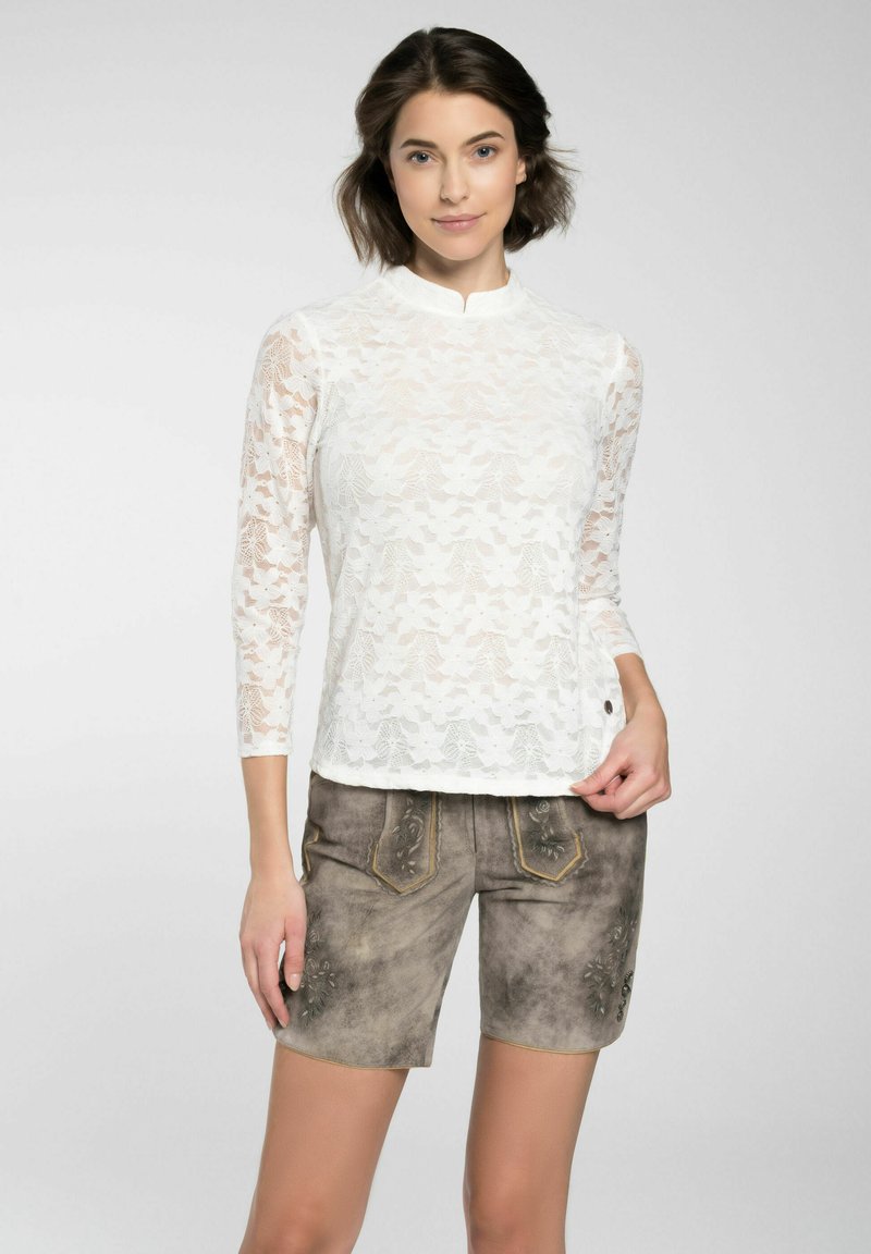 Weißes Spitzenoberteil mit langen Ärmeln und hohem Kragen, kombiniert mit grauen Shorts, die mit floralen Stickereien und kontrastierenden Nähten verziert sind.