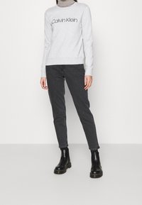 Šedá mikina s logem "Calvin Klein", černé skinny džíny a černé kotníkové boty. Pod mikinou pruhovaný rolák.