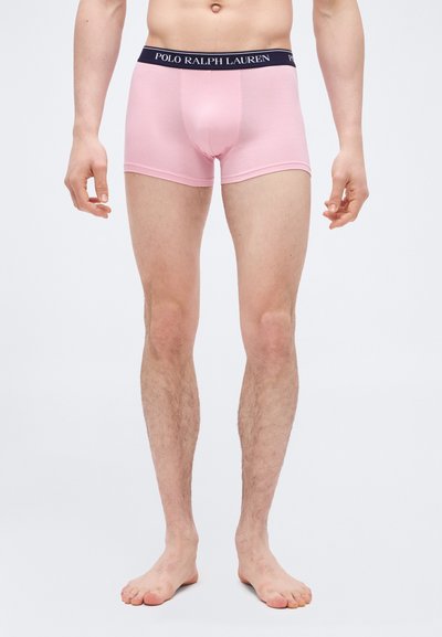 Άνδρας που στέκεται ξυπόλυτος φορώντας ανοιχτό ροζ boxer briefs Polo Ralph Lauren με μαύρη μέση και λογότυπο.