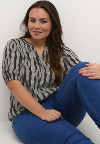 Blouse à motif noir et blanc avec des manches courtes et un col en V, associée à un jean bleu. Tissu lisse avec une coupe décontractée.