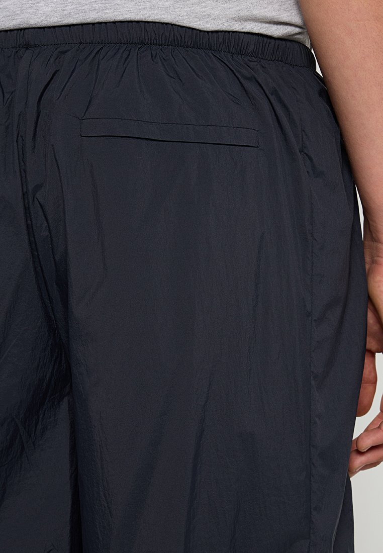 Zwarte lichtgewicht shorts van nylon, met een elastische tailleband en een enkele achterzak. Soepele textuur met een lichte glans.