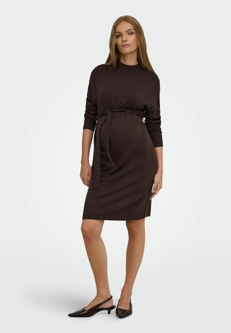 Femme enceinte portant une robe en maille marron foncé à manches longues avec une ceinture à la taille et des chaussures slingback noires à talons bas, debout avec assurance.