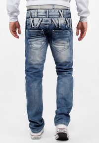 Jean en denim bleu clair avec une texture délavée, cinq poches, des coutures décoratives et plusieurs passants de ceinture sur la taille.