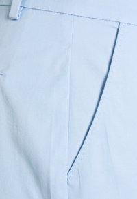 Jasnoniebieska tkanina o fakturowanym splocie, wyposażona w boczną kieszeń i precyzyjne przeszycia. Odpowiednia do noszenia na co dzień.