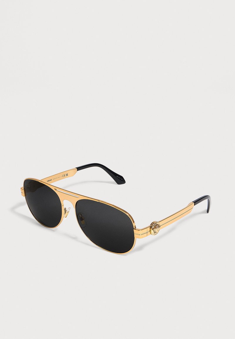 Γυαλιά ηλίου aviator με χρυσό πλαίσιο, μαύρους φακούς και μαύρα άκρα στα μπράτσα, εμφανιζόμενα σε απλό φωτεινό φόντο.