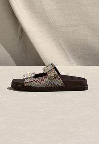 Sandale ouverte à enfiler avec des brides en tissu à motif zigzag dans des tons bleus, rouges et beiges, et une semelle noire, vue de côté sur un fond neutre.