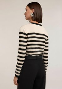 Randig tröja i krämvitt och svart, med långa ärmar, rund halsringning och en figursydd design. Bärs med svarta skräddarsydda byxor.