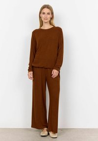 Ensemble de loungewear marron comprenant un haut à manches longues et un pantalon à jambes larges, fabriqué à partir d'un tissu doux et texturé avec une taille élastique.