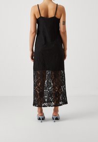 Black lace midi dress with a sheer lower panel, adjustable spaghetti straps, and a fitted bodice. Features a floral pattern throughout.