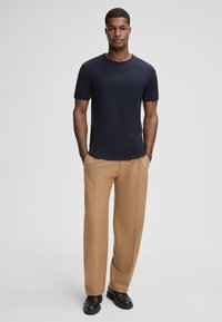 T-shirt blu navy a maniche corte con scollo rotondo, abbinato a pantaloni leggeri beige e scarpe scure. Tessuto morbido, vestibilità rilassata.