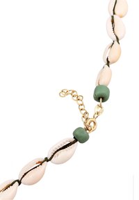 Bracelet composé de coquillages blancs de cauris enfilés sur un fil foncé, agrémenté de perles vertes et d'un fermoir chaîne dorée avec des maillons d'extension.