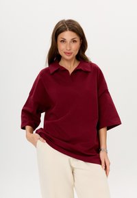 Bordeaux poloshirt met korte mouwen en een kraag, gemaakt van zachte stof, gecombineerd met lichtbeige broeken met een relaxte pasvorm.