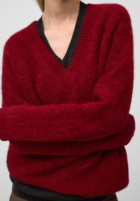 Czerwony, puszysty sweter z dekoltem w serek, z kontrastującym czarnym prążkowanym kołnierzykiem. Miękka tekstura i luźny krój z długimi rękawami.