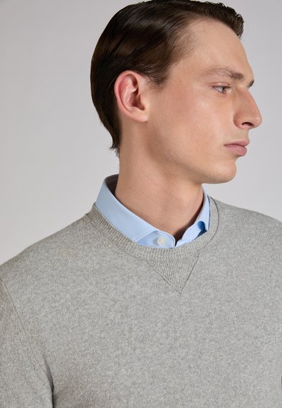 Suéter gris claro con diseño de escote en V, hecho de tela suave. Usado sobre una camisa azul claro con cuello, resaltando la textura en capas.