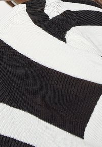 Gestreifter Strickpullover in Schwarz und Weiß, mit einer strukturierten Stoffoberfläche, locker sitzend und mit kontrastierenden breiten Streifen.